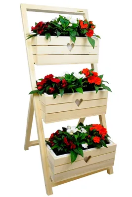 A wooden plant stand with three tiers, each holding a planter box filled with red and white flowers.