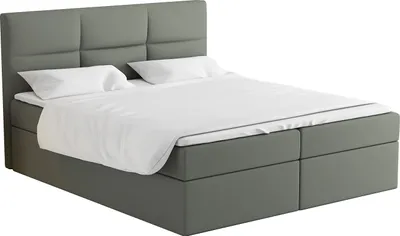 A studio shot of a gray boxspring bed with white bedding.