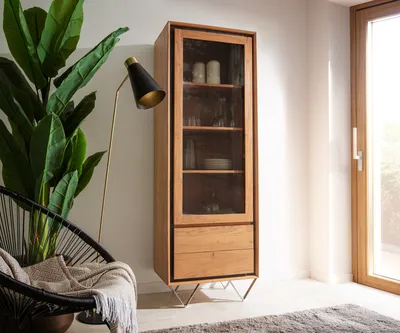 A modern living room scene featuring a wooden display cabinet, a black chair with a blanket, and a floor lamp.