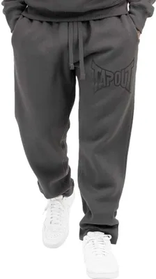 A person wearing grey sweatpants with a black logo on the left leg and white sneakers.