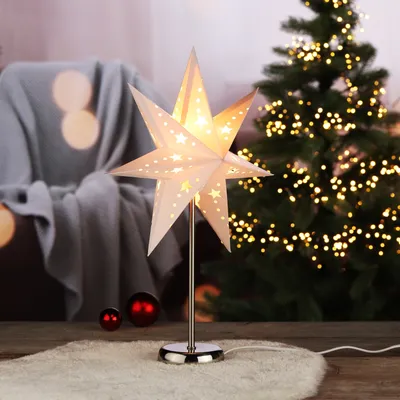 A star-shaped lamp sits on a fluffy rug in front of a Christmas tree and a draped chair.