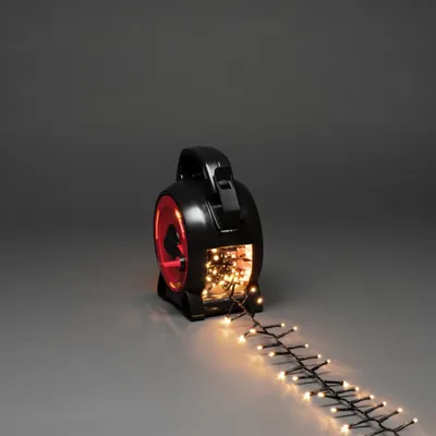 A black reel with red accents, holding a string of warm white LED lights, with some lights unspooled onto a gray surface.