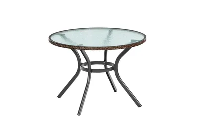 A round outdoor table with a glass top and a woven base, shown against a white background.