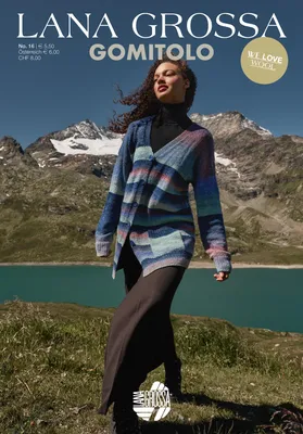 A woman walks in a mountainous landscape with a lake in the background, wearing a striped cardigan.