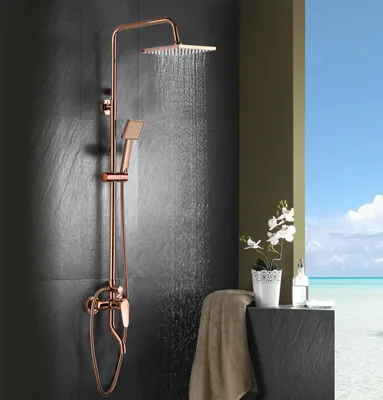 A rose gold shower system is shown in a modern bathroom setting with a view of the ocean and sky in the background.