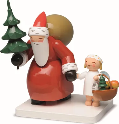 A wooden figurine of Santa Claus carrying a Christmas tree and a sack, accompanied by a small angel holding a basket of fruit and a miniature tree.