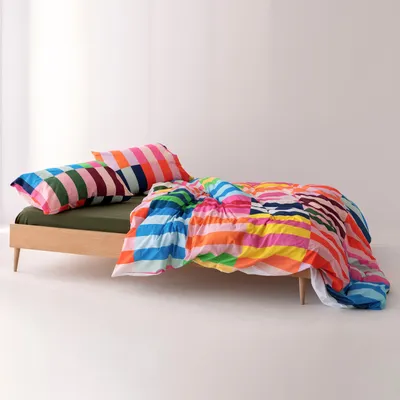 A colorful striped duvet cover and pillow are laid out on a simple wooden bed frame.