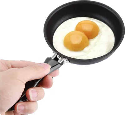 A hand holding a mini frying pan with two fried eggs.