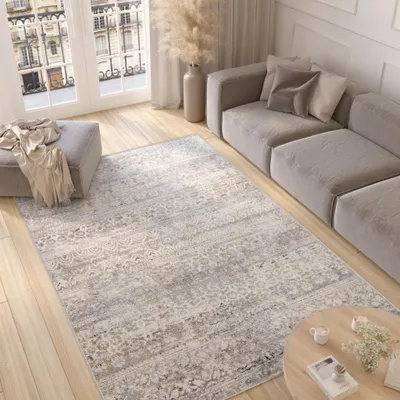 A modern living room with a gray sectional sofa, a patterned rug, an ottoman, and a coffee table.