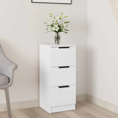 A white three-drawer cabinet with a vase of white lilies on top, placed next to a grey chair in a room.