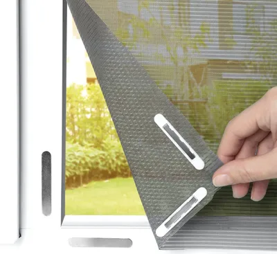 A hand is shown attaching a gray mesh mosquito net with white magnetic fasteners to a window frame.