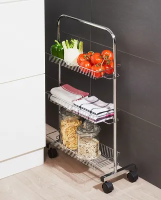 A kitchen trolley with three shelves filled with food and kitchen items, placed next to a white cabinet and a dark tiled wall.