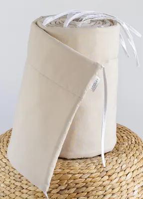 A rolled-up baby bed bumper on a woven mat.