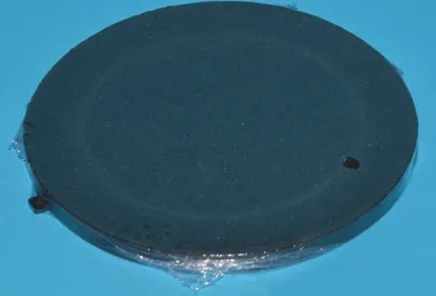 A dark circular object covered in plastic wrap, resting on a light blue surface.