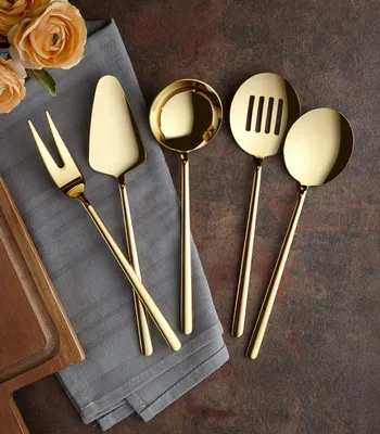 A set of gold-colored kitchen utensils laid out on a gray napkin, with flowers in the background.