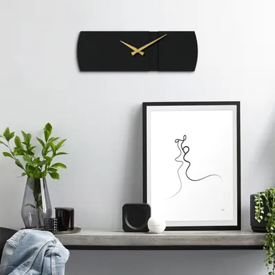 A black wall clock with gold hands is mounted on a white wall above a shelf with decorative items.