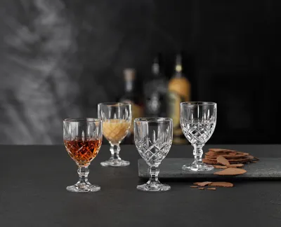Four liqueur glasses filled with different liquids and chocolate shavings on a dark surface.
