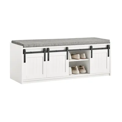 A white shoe bench with a gray upholstered seat and sliding barn doors, featuring open shelving for shoes.