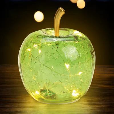 A green glass apple with embedded LED lights sits on a wooden surface.