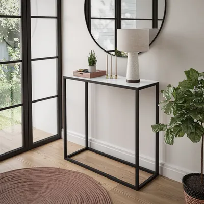 A modern console table with a marble top and black metal frame, decorated with a lamp, a small plant, and candles. It is placed in a well-lit room with large windows and a round rug.
