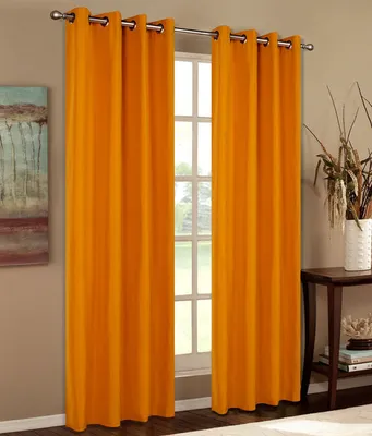 Two orange curtains hang on a window rod, framing a window with white mullions. A painting hangs on the wall to the left, and a wooden table with decorative items is on the right.