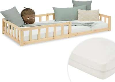 A wooden children's bed with guardrails, shown with pillows and a blanket.
