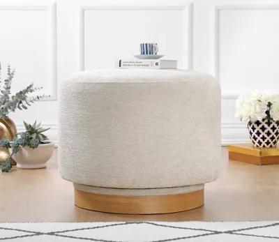 A cream-colored round ottoman with a wooden base is shown in a well-lit room with decorative plants and flowers in the background.
