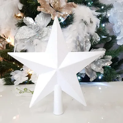 A white glitter star tree topper is shown in front of a decorated Christmas tree.