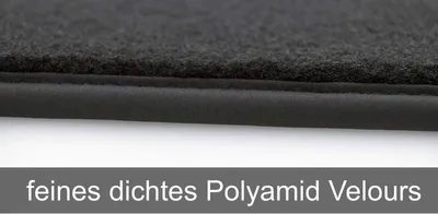 A close-up view of the edge of a black car floor mat, showing the texture of the velour material and the stitched edging.