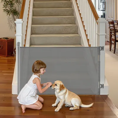 A child and a puppy interact at the bottom of a staircase, separated by a retractable safety gate.