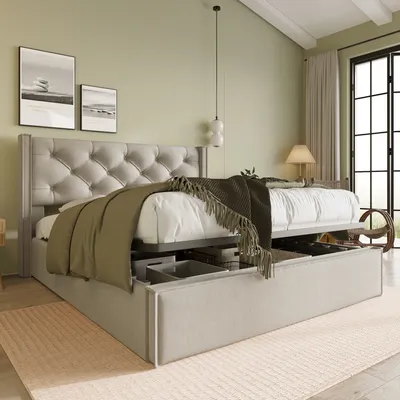 A bedroom scene featuring a hydraulic storage bed with a tufted headboard, blankets, and pillows. The bed is open, revealing storage compartments underneath. A lamp and a window with curtains are visible in the background.