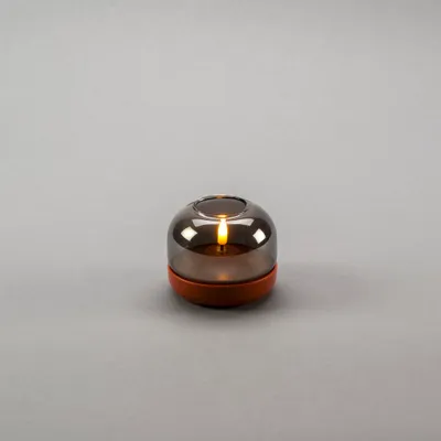 A battery-operated LED candle with a smoky glass shade and a terracotta-colored base is displayed on a plain gray background.