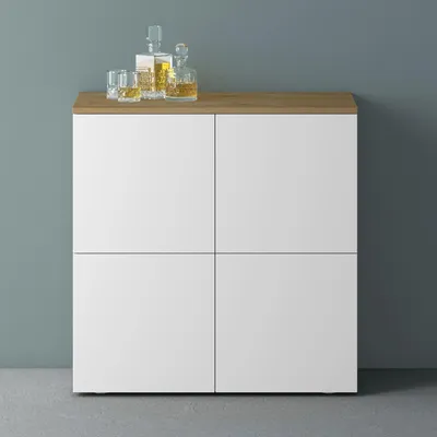 A modern sideboard with a wood-effect top and white doors against a gray wall.