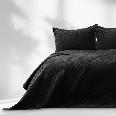 A black quilted bedspread with two pillows on a bed, with soft shadows on the wall behind.