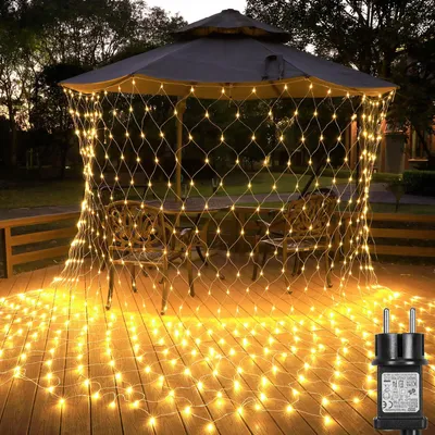 A net of fairy lights is draped over a gazebo and illuminates a wooden deck with chairs and a table.