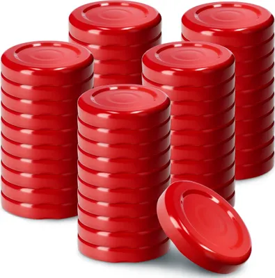Several stacks of red lids for canning jars are arranged on a white background, with one lid lying on its side in the foreground.