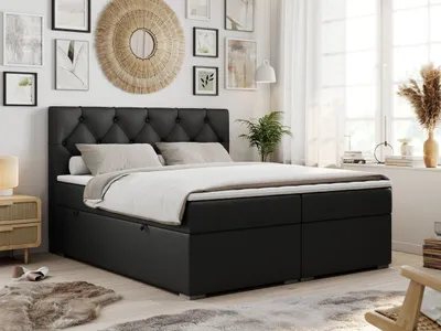 A bedroom scene with a large black boxspring bed as the focal point, decorated with pillows and a duvet. The room is furnished with a bedside table, a rug, and artwork on the wall, suggesting a comfortable and stylish living space.