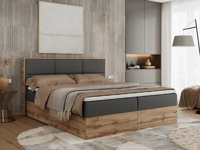 A bedroom scene featuring a large boxspring bed with a dark gray upholstered headboard and a wooden frame. The bed is made with beige and brown linens and a textured throw blanket. The room has modern gray cabinetry and a large abstract painting on the wal