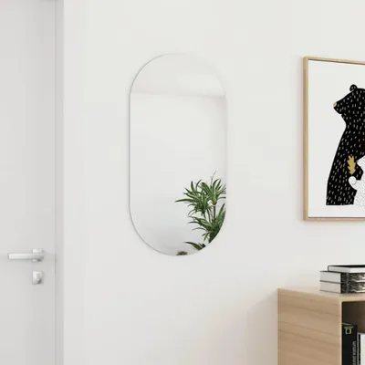 A modern oval mirror hangs on a white wall next to a door and a framed picture.