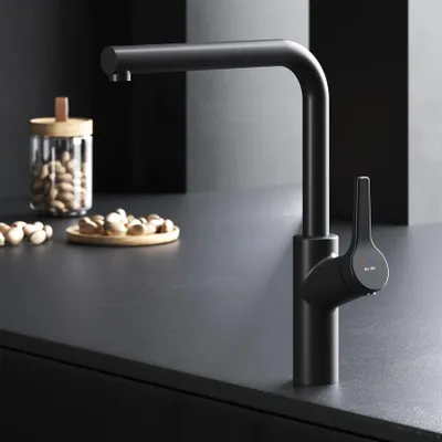 A black kitchen faucet is shown on a dark countertop, with a jar of nuts and a small plate of nuts in the background.