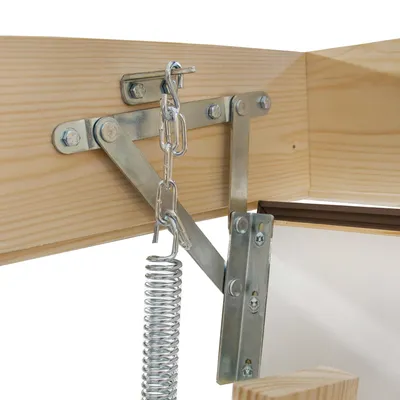 Close-up of a metal mechanism with a spring attached to a wooden beam, likely part of a retractable attic ladder.