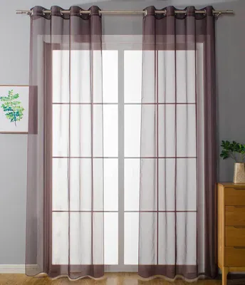 A pair of sheer brown curtains hangs in front of a window with a grid pattern. A framed picture hangs on the wall to the left, and a wooden dresser with a plant on top is visible to the right.