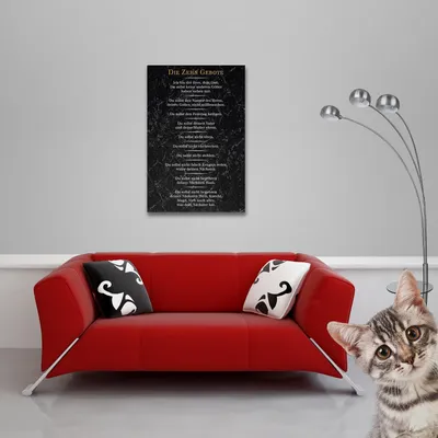 A red sofa with two pillows is placed in front of a gray wall with a black poster hanging on it. A floor lamp is to the right of the sofa, and a cat is peeking from the right side of the image.