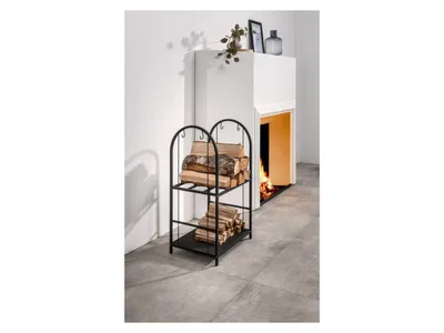 A black metal firewood rack with two shelves, filled with logs, is placed next to a modern fireplace with a fire burning inside.