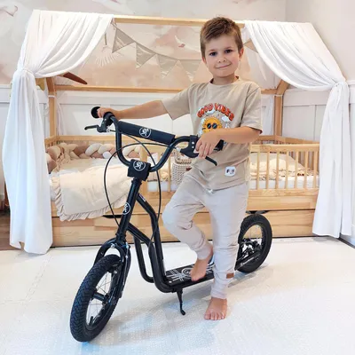A young boy is posing with a scooter in a bedroom.