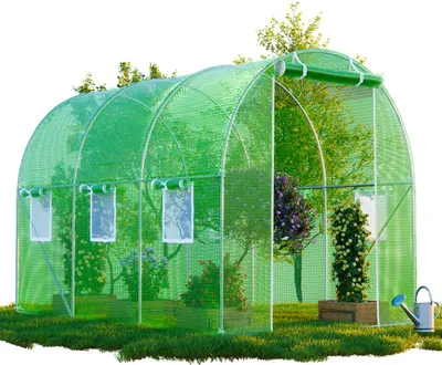A green greenhouse with plants inside, set in a grassy outdoor environment with a watering can nearby.