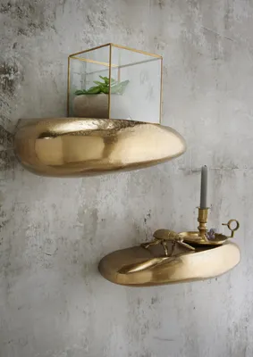 Two decorative shelves are mounted on a textured gray wall. The top shelf holds a glass terrarium with a small plant. The bottom shelf holds a decorative bowl with a brass beetle sculpture and a candle holder with a candle.