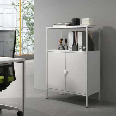 A white metal cabinet with two doors and an open shelf above, placed in an office setting.