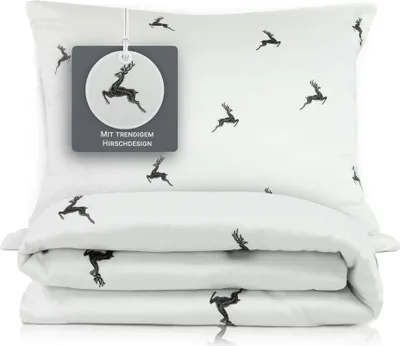 A white pillow and folded duvet cover with a repeating pattern of black deer silhouettes, presented on a white background.