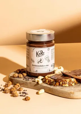 A jar of nut spread with nuts and crackers on a wooden board.